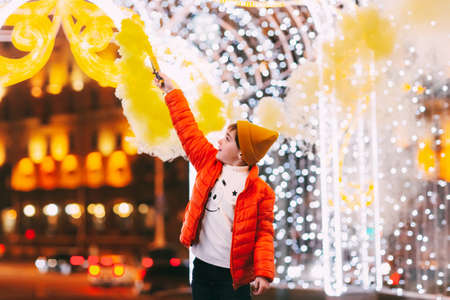 A teenage boy with a smoke bomb in his hands during the celebration of Christmas or New Year against the background of city illuminationの写真素材