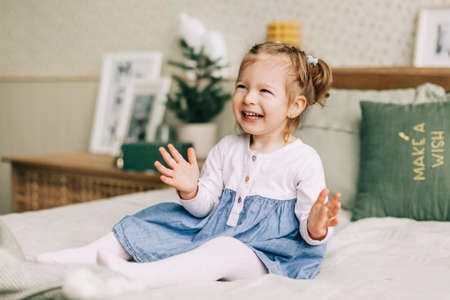 A beautiful little girl is sitting on the bed and laughing, the child is happy about Christmas or New year. Childhood, Christmas mood, time of miraclesの写真素材