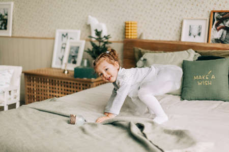 A happy girl is playing on the bed on Christmas morning in a room decorated for Christmas or New Year. Childhood, festive morning, Christmas moodの写真素材