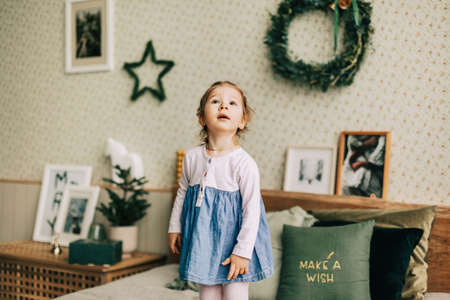 A happy girl is playing on the bed on Christmas morning in a room decorated for Christmas or New Year. Childhood, festive morning, Christmas moodの写真素材