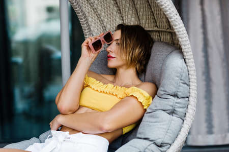 A woman sitting on a wicked swing on the track and holding sunglasses in her handの写真素材