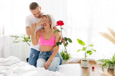 A young man covers his wifes eyes with his hand, makes a surprise, congratulates her on Valentines Day or anniversaryの写真素材