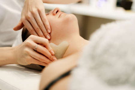 Neat female hands of a massage therapist-cosmetologist do massage with a gouache scraper made of jade in the shape of a heartの写真素材