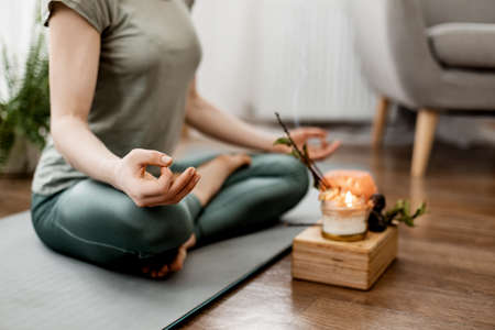 Young relaxed woman doing yoga at home with candles and incense, close-up of handsの写真素材