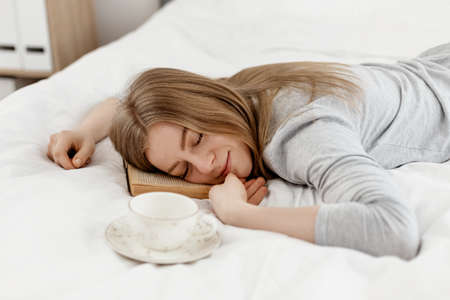 A young girl lies with her eyes closed, holding a book in her hands, lying on the bed at homeの写真素材