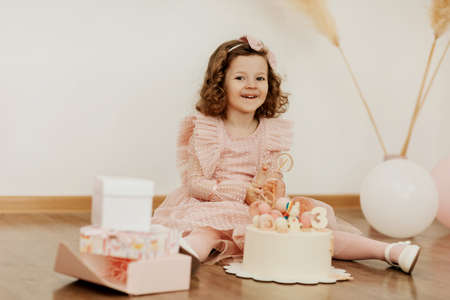 A cute little girl is sitting on the floor with a cake and gifts on her birthday and laughing merrilyの写真素材