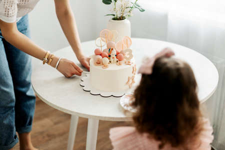 Mom cuts a piece of cake for her daughter during a birthday celebration at homeの写真素材