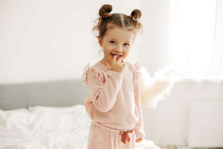 Portrait of a happy girl standing on the bed in the bedroom in the morning after waking upの写真素材