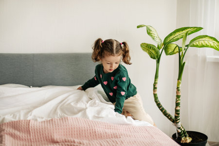 A little girl with two ponytails makes her bed in the morning after waking upの写真素材