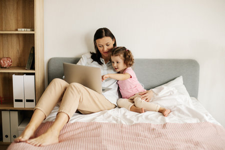 A sweet mom with her little daughter watches a video or movie on a laptop, or works from homeの写真素材