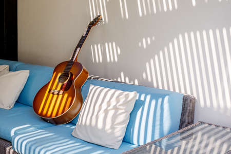 An acoustic guitar stands on a blue sofa next to a pillow on the terraceの写真素材