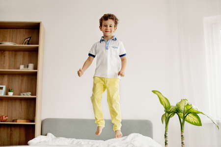 A little boy jumps on his bed in the bedroom and laughs.