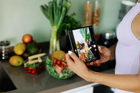Close-up of a girl's hand taking a photo on her phone. A young woman, a culinary blogger, cooks in...