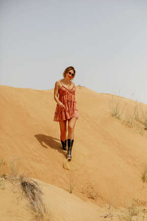 A lonely girl walks down the sand dunes. A Caucasian woman in a short dress descends from a mountain in the desert.の写真素材