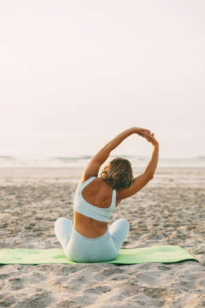A young woman practices yoga in the lotus position on the shore of the poria, rear view.の写真素材