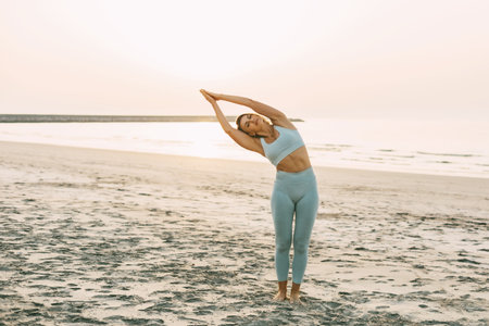 A slender girl practices yoga on the beach at sunset, performs asanas.の写真素材