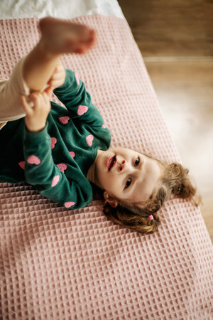 A cute little girl is lying on the bed with her leg raised and straightens her pantiesの写真素材