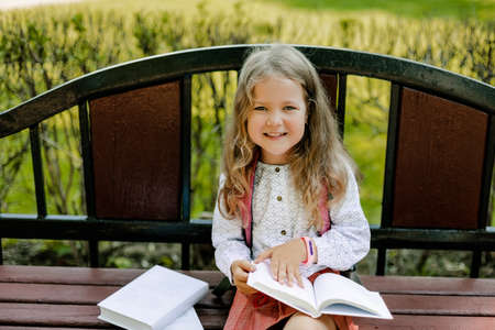 Portrait of a pretty schoolgirl girl sitting with books on a bench in the park or near the schoolの写真素材