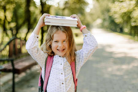 A charming little girl with a book on her head, on the first day at school or kindergarten. The concept of training and educationの写真素材