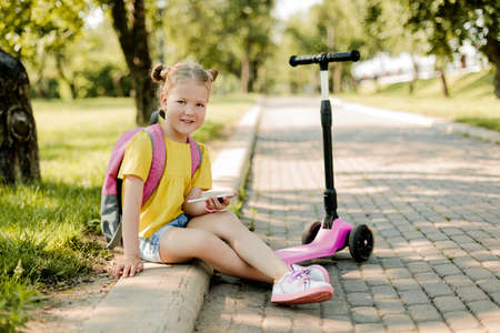 A pretty girl is resting on the way from school, playing on the phone or texting friends.. Modern technology, back to schoolの写真素材