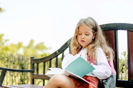 A cute thoughtful schoolgirl is sitting on a bench with books. Back to school, lesson schedule, elementary schoolの写真素材