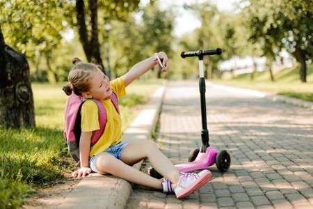 Portrait of a little beautiful schoolgirl girl using a mobile phone and taking a selfieの写真素材