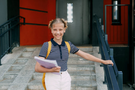 A smiling teenage girl with a backpack and a folder in her hands goes down the stairs, hurries to school. Back to school, high schoolの写真素材