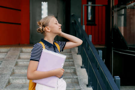 A smiling teenage girl with a backpack and a folder in her hands goes down the stairs, hurries to school. Back to school, high schoolの写真素材