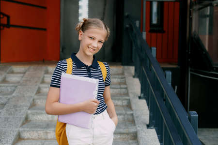 A smiling teenage girl with a backpack and a folder in her hands goes down the stairs, hurries to school. Back to school, high schoolの写真素材