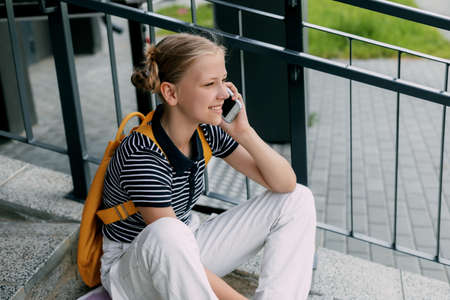 A beautiful girl is sitting on the stairs at school in between classes and talking on the phoneの写真素材
