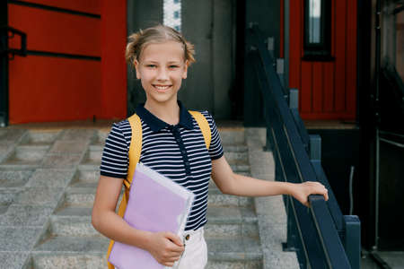 A smiling teenage girl with a backpack and a folder in her hands goes down the stairs, hurries to school. Back to school, high schoolの写真素材