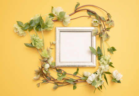 Flat lay composition of the beautiful empty antique frame, decorated with ranunculus flowers, on the textured yellow wall. Copy text for a menu, reception, party poster, or wedding invitation.の写真素材