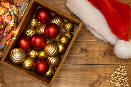 Wooden box with Christmas tree balls or baubles for festive decor and red Santa Claus hat on wooden background.の写真素材