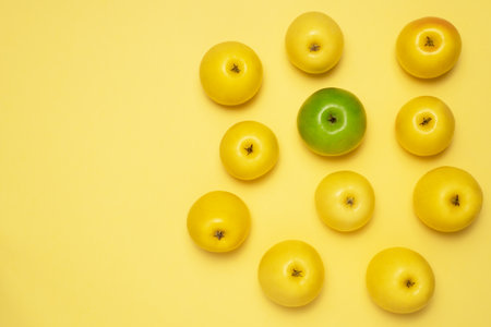 One green apple among the yellow. Apples on yellow background. Sweet and delicious fruits. One different among the like concept.の写真素材