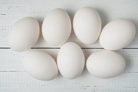 White raw chicken eggs on white wooden boards background.