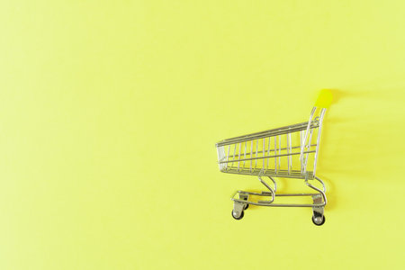 Empty shopping cart with yellow handle on light yellow background.の写真素材