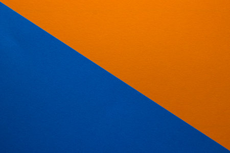 Background of blue and orange paper divided diagonally. Sheets of blank orange and blue paper with fine texture, close up.の写真素材