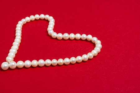 Pearl beads in the shape of a heart on red background. Valentines day or Womens day concept.の写真素材