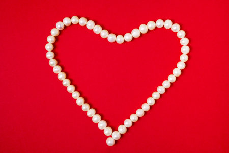 Heart of beads from white pearls on red background. Valentines day concept.の写真素材