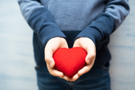 Child boy holding red heart symbol in hands. Background for Mothers day. Kindness, love and charity concept.