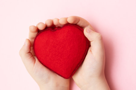 Little child hands holding soft red heart on pink background, close up. Kindness, love and charity concept.の写真素材