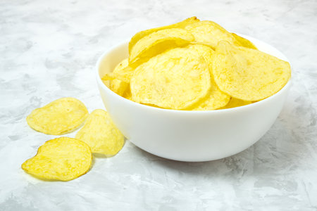 Golden solted natural potato chips in white ceramic bowl on concrete background.の写真素材