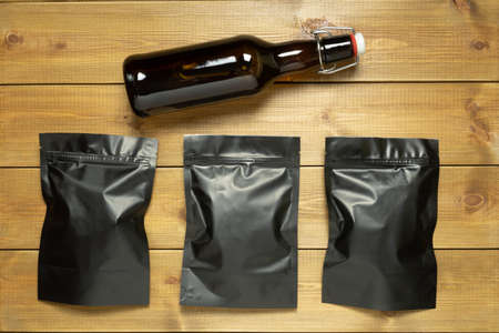 Bottle of beer and black packages of assorted snacks on wooden table.