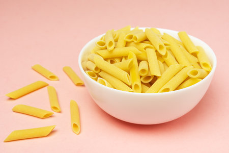 Penne italian pasta in white ceramical bowl on pink background with copy space.の写真素材