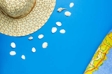 Summer vacation layout. Terry towel with map, hat and seashells on blue background. Tourism and relaxation concept. Copy space.の写真素材