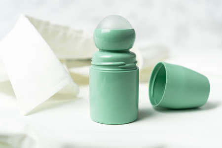 Green bottle of roll on antiperspirant deodorant lying on background of white blouse or shirt....