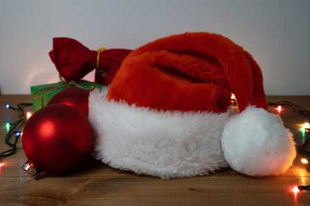 Christmas decorations. Santa Claus red hat, red Christmas glass balls and gifts on wooden table.の写真素材