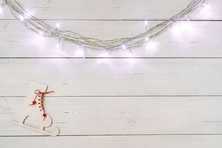 Christmas garland lights and wooden skates toy on white wooden boards background.の写真素材
