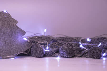 Christmas or New year decoration with felt fir tree and cozy knitted scarf with pompoms in the light...