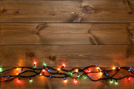 Glowing multicolored electric garland at the bottom of the natural wood boards background, copy...